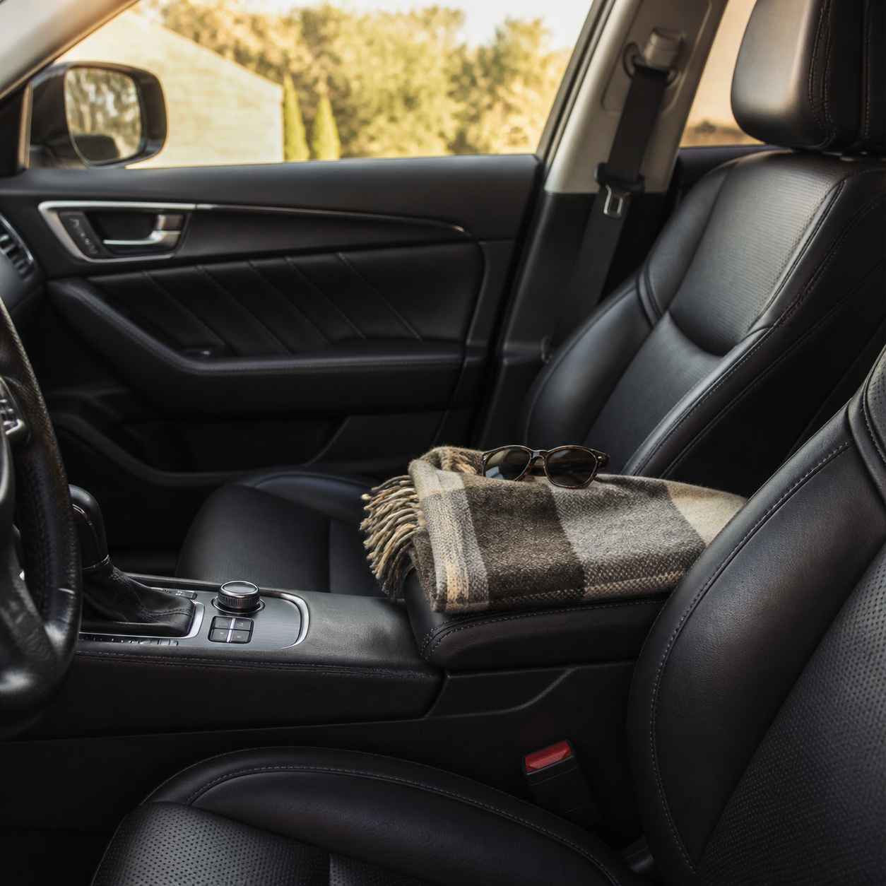 Lived-in black leather car interior with a folded wool blanket and sunglasses